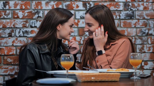 Young and cheerful girls gossip and whisper to each other while sitting in a cafe