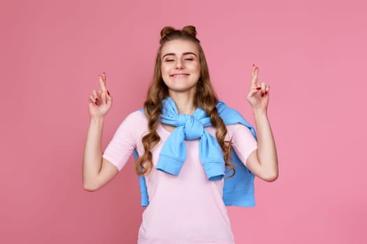 beautiful caucasian curly woman with finger crossed gesture isolated on pink background.