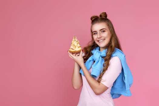 Excited beautiful woman eating with satisfation pizza slice on pink background. copy space