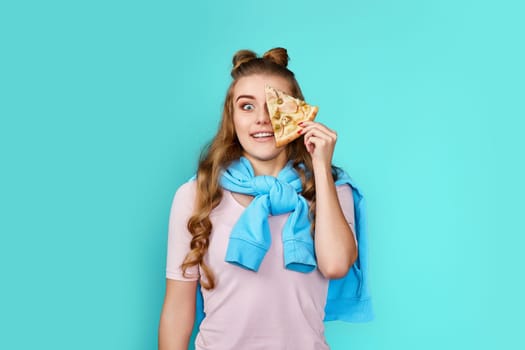 amazed woman covering her eyes with slice of fresh pizza on blue background.