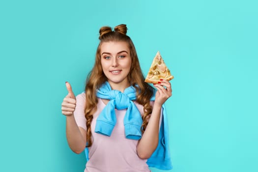 young woman eating delicious pizza slice and showing ok gesture on blue background