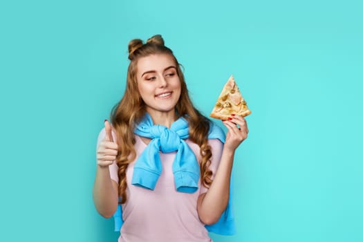 young woman eating delicious pizza slice and showing ok gesture on blue background