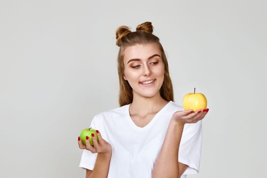smiling woman holding green and yellow apples on gray background. healthy food
