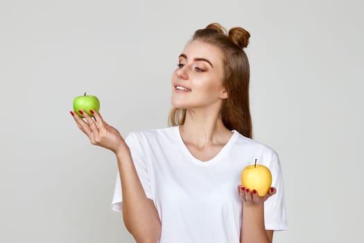 smiling woman holding green and yellow apples on gray background. healthy food
