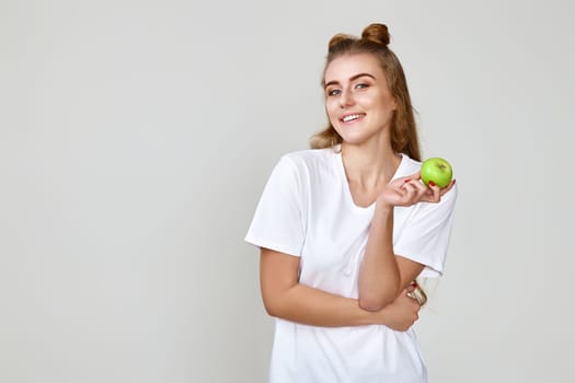 happy brunette woman holding green apple isolated on studio background. copy space