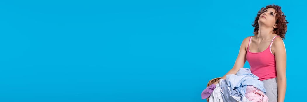 A very tired woman , carries a heavy wicker basket with washed clothes. Overworked woman with dark and curly hair. Monotonous housework. . Panoramic view of girl with empty blue background.