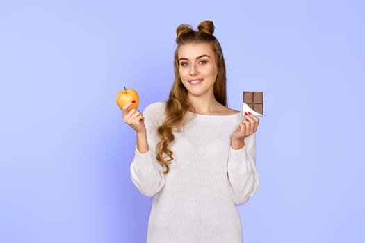 young happy woman making choice between healthy apple and unhealthy chocolate isolated on pastel violet background. Delicious and harmful