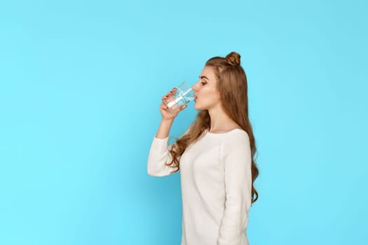 beautiful woman drinks water from a glass on blue background. copy space
