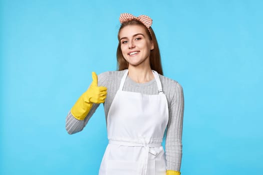 beautiful happy woman in yellow rubber gloves and cleaner apron showing ok sign isolated on blue background. cleaning