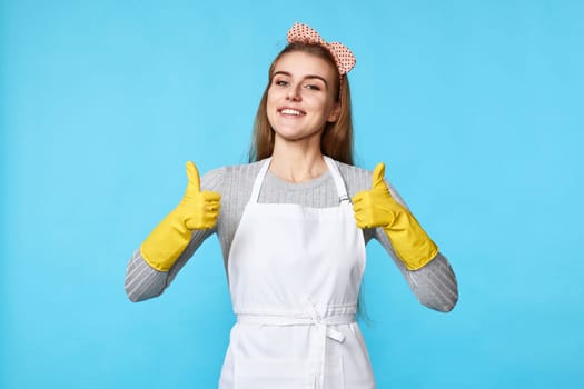 beautiful happy woman in yellow rubber gloves and cleaner apron showing ok sign isolated on blue background. cleaning