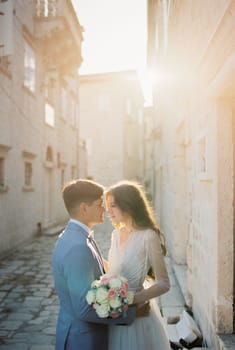 Groom almost kisses bride with a bouquet on a narrow street of an old town. High quality photo