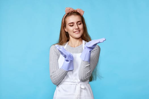 pretty woman in rubber gloves and cleaner apron on blue background. cleaning