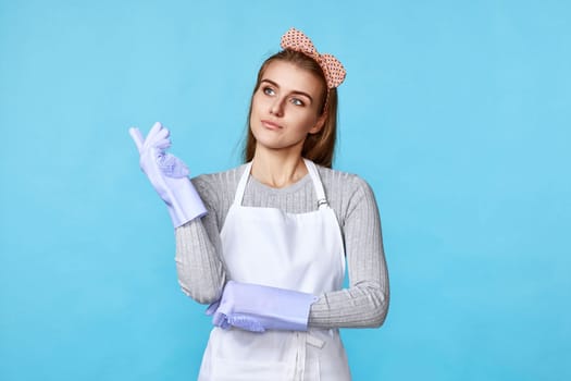 beautiful woman in violet rubber gloves and apron holding index finger up with new idea on blue background. cleaning