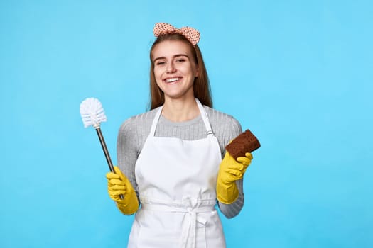 happy woman in rubber gloves cleaning with sponge and toilet brush on blue background.