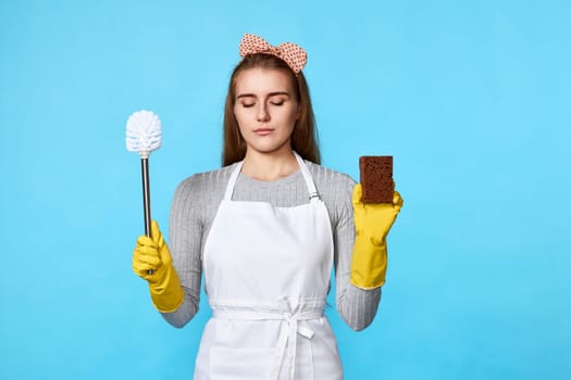 calm woman in rubber gloves cleaning with sponge and toilet brush on blue background.