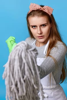 diligent woman in rubber gloves shows the mop to the camera on blue background. cleanliness everywhere