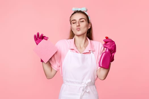 caucasian woman in pink rubber gloves and cleaner apron with cleaning rag and detergent sprayer kisses