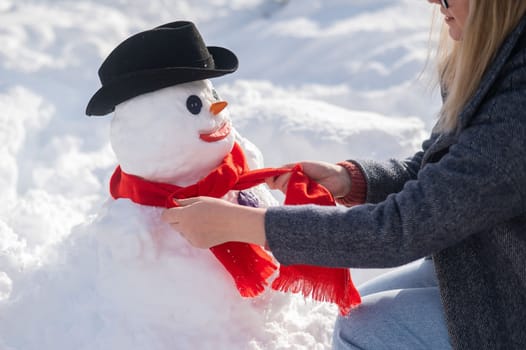 Caucasian woman sculpts a snowman from the snow. The carrot is the place of the nose