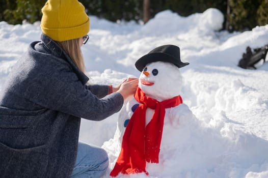 Caucasian woman sculpts a snowman from the snow. The carrot is the place of the nose