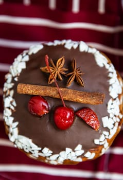 A traditional paska decorated with white and dark Swiss chocolate and cherries, cinnamon and star anise stands on a cherry striped apron. Easter holiday, top view and close up