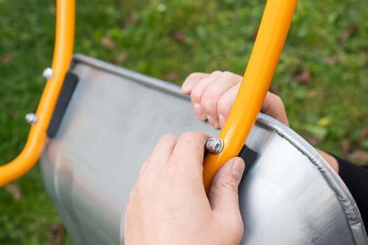 A metal wheelbarrow stands on the street, a man twists a new wheelbarrow for work, twists bolts and nuts