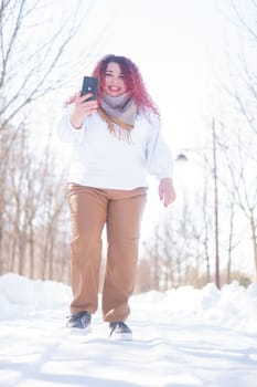 Portrait of a smiling plump red-haired woman taking a photo on a smartphone on a walk in winter