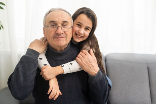 Smiling granddad hugging girl while sitting on sofa.