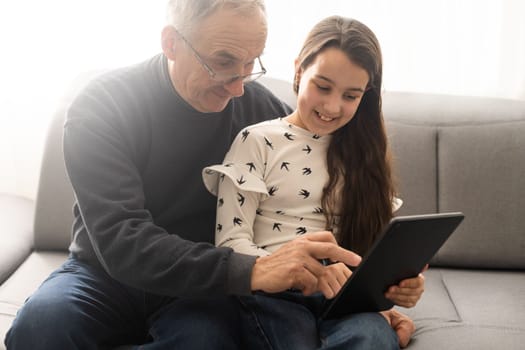 Senior man with his grandchild looking together on photos in tablet.