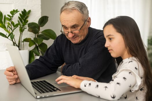 Portrait of grandfather and granddaughter doing homework with laptop