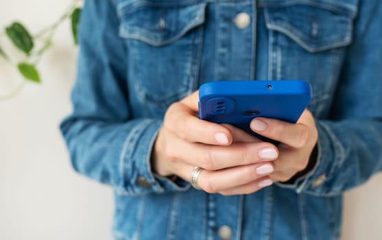 A girl in a denim shirt holds a smartphone in her hands. The concept of working online, freelancing, correspondence, chat. Close-up