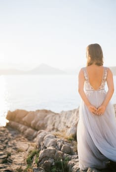 Bride stands on a rocky shore and looks at the sea. Back view. High quality photo
