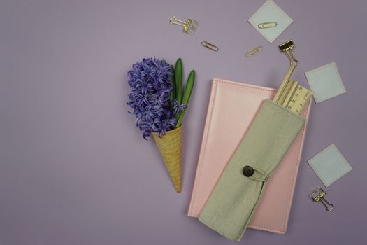 On the table is a pink notebook, stationery and a hyacinth flower in a waffle cone. Office of business lady Flatley. A freelancer's workplace on a public holiday.