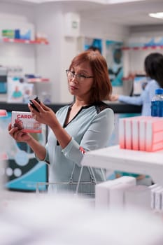 Elderly woman holding cardiology pills package and looking at bottle of medicine, buying medical products from pharmacy. Reading medicaments box leaflet before taking supplements.