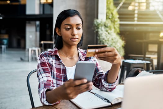 Ordering textbooks online. a young female student using a cellphone and credit card outside on campus