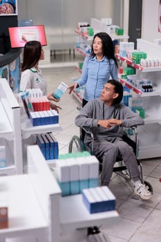 Male client in wheelchair talking to pharmacist about prescription medicine and pharmaceutical products. Customer with disability buying medicinal supplements and vitamins, box of drugs.