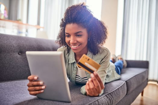 Paying the bills with a smile on my face. a cheerful young woman doing online shopping while lying on a couch at home during the day