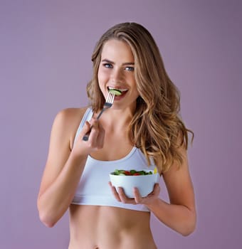 Respect your body, its the only one you have. Studio shot of a healthy young woman eating a salad against a purple background