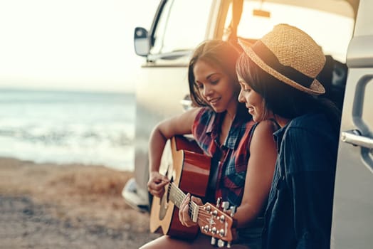 The song that would always remind them of that summer. a young woman playing a guitar on a road trip with her friend
