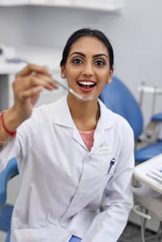 Open wide. Portrait of a young female dentist holding a surgical instrument