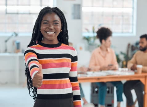 Portrait of a young happy african american businesswoman showing a thumbs up in an office at work. Cheerful black female businessperson showing support with a hand gesture.