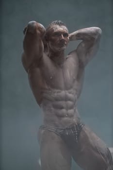 Studio shot of a muscular man. A muscular man shows off his perfect shirtless torso with his hands behind his head. Professional bodybuilder posing concept