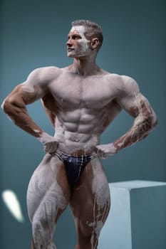 Studio shot of a muscular man. Adult bodybuider without clothes put his hands on his hips and looks to the side. Professional male modeling posing concept