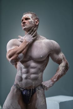 Studio shot of a muscular man. Young handsome athletic caucasian guy with beautiful naked torso looking away while posing shirtless isolated over grey background. Sports workout concept