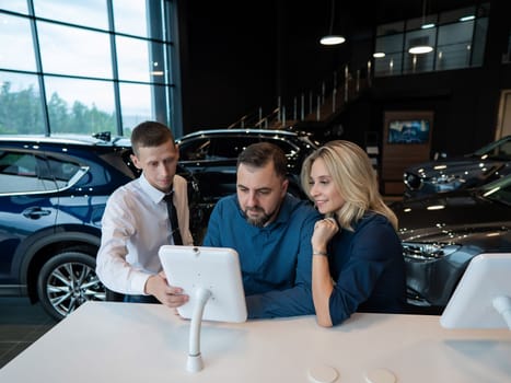 Caucasian married couple chooses a car in a car dealership on digital tablets
