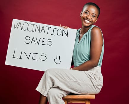 African american covid vaccinated woman showing and holding poster. Portrait of smiling black woman isolated against red studio background with copyspace. Model promoting corona vaccine with sign.