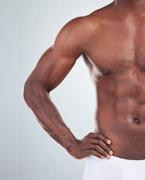 Closeup of one African American fitness model posing topless in a underwear and looking muscular. Confident black male athlete isolated on grey copyspace in a studio wearing boxers showing his sixpac.