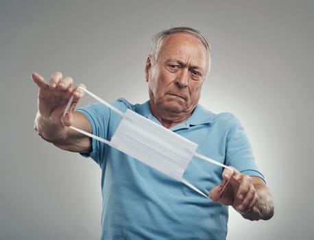 I hope this does a good job of protecting me. an older man looking at a face mask in confusion in a studio against a grey background