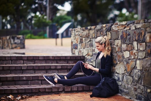 Putting on some music to motivate her. a sporty young woman listening to music while sitting outside