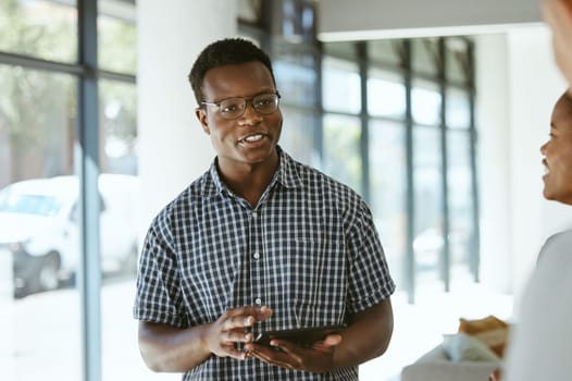 Young happy african american businessman holding a digital tablet while talking with colleagues in an office at work. Male boss wearing glasses and talking to coworkers in a meeting at work.