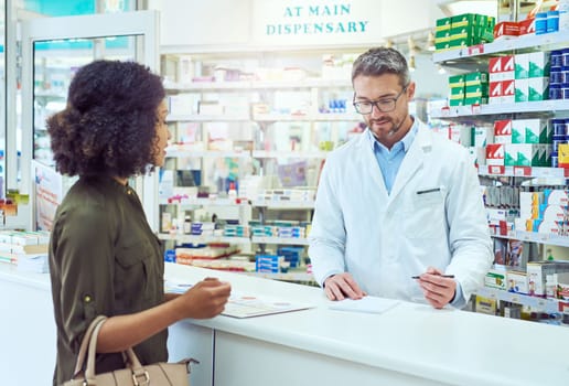 Filling out her prescription. a handsome mature male pharmacist helping a female customer in the pharmacy